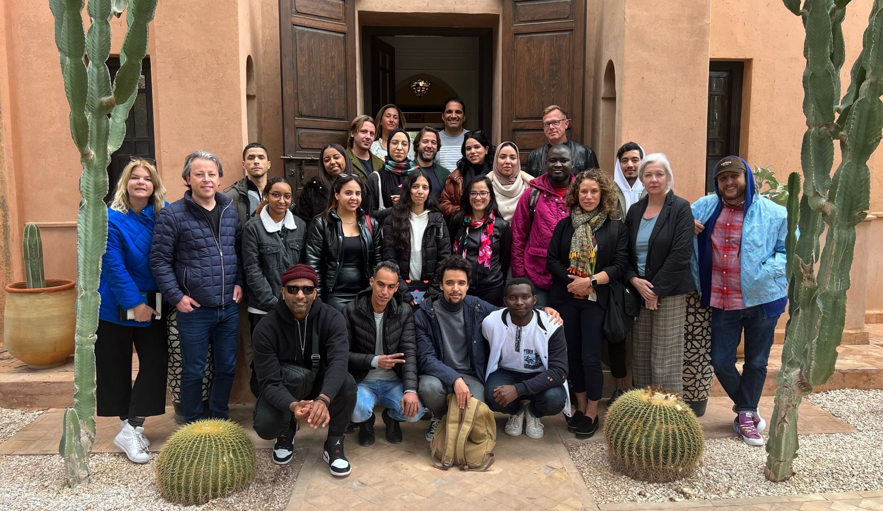 A large group of creatives and mentors gathered in front of a riad doorway framed by cacti